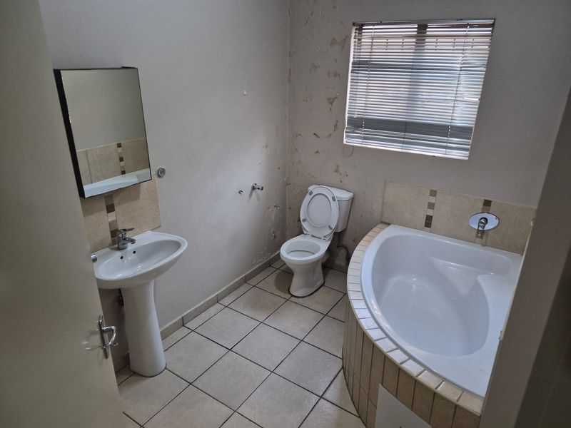 A bathroom featuring a pedestal basin, toilet, and built-in bathtub, currently requiring wall repairs and cosmetic updates.