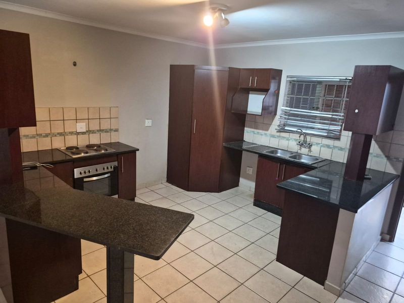 A functional kitchen featuring dark wood cabinetry, granite countertops, a built-in oven and hob, and tiled flooring throughout.