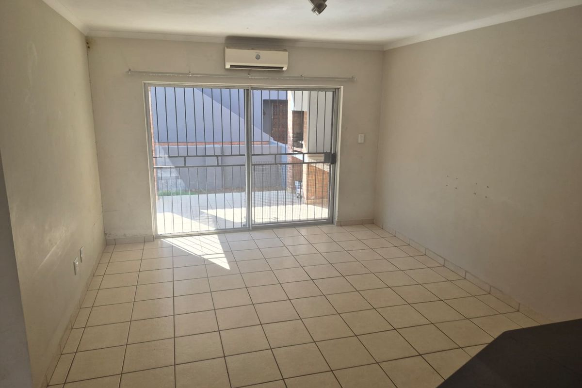 An empty living room featuring tiled flooring, a wall-mounted air conditioning unit, and a sliding glass door with a security gate leading outside.