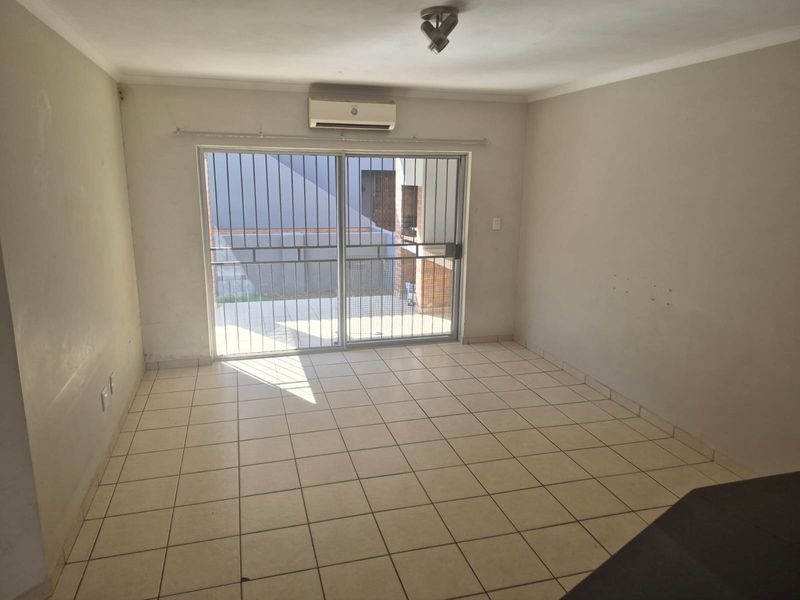 An empty living room featuring tiled flooring, a wall-mounted air conditioning unit, and a sliding glass door with a security gate leading outside.