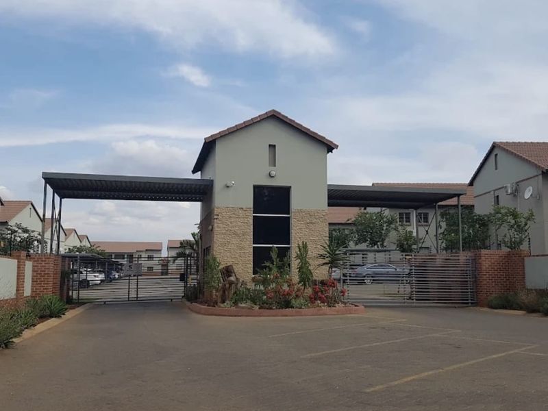 The main entrance and security gatehouse of the apartment complex, featuring a paved driveway, metal security gates, and stone-clad architectural detailing.
