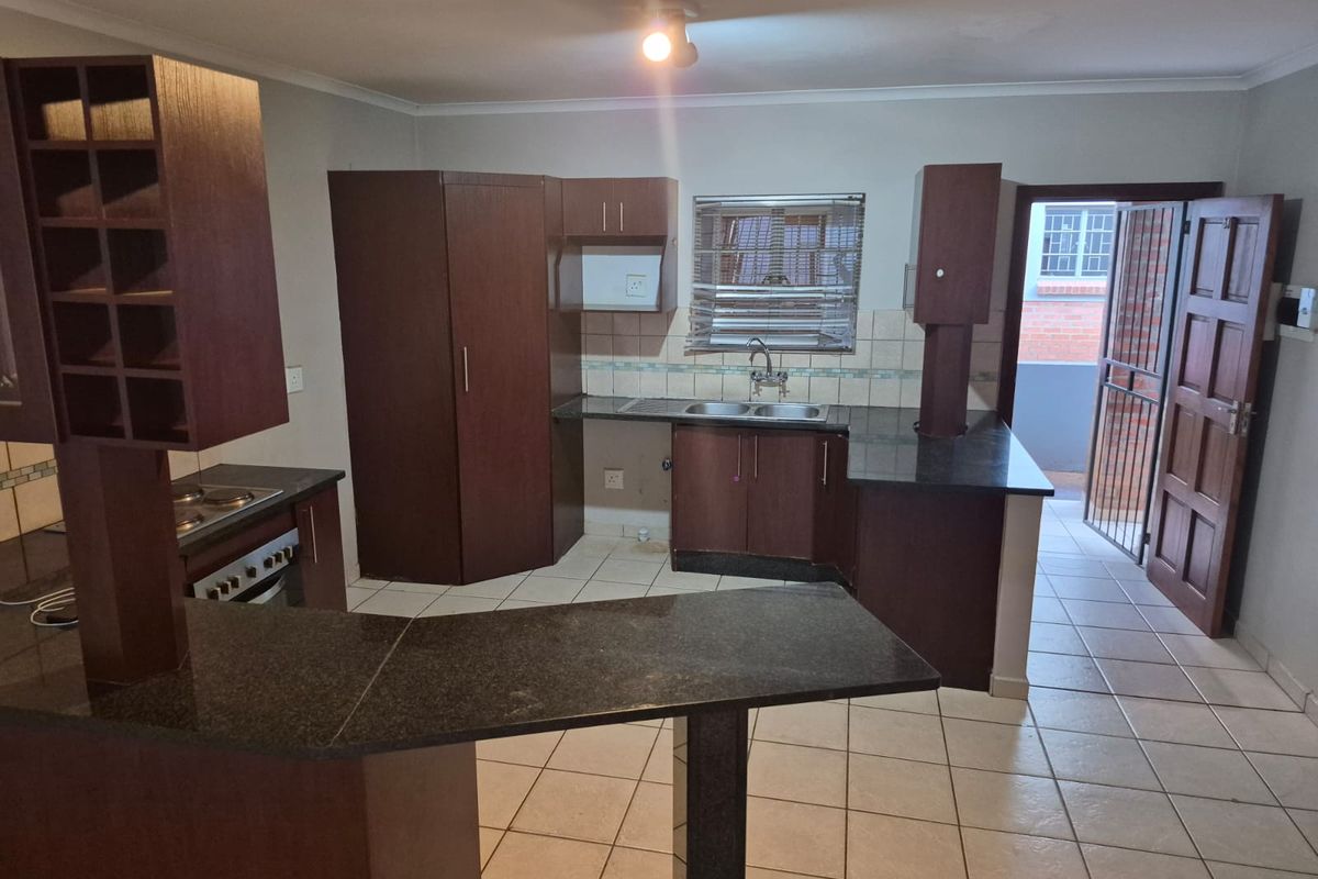 A functional kitchen featuring dark wood cabinetry, granite countertops, a built-in oven and hob, and tiled flooring with direct access to an exterior area.
