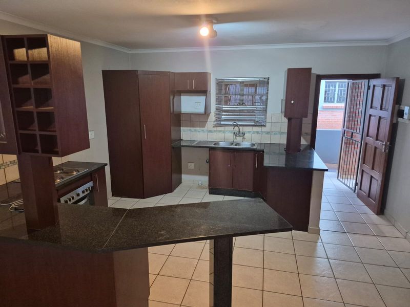 A functional kitchen featuring dark wood cabinetry, granite countertops, a built-in oven and hob, and tiled flooring with direct access to an exterior area.