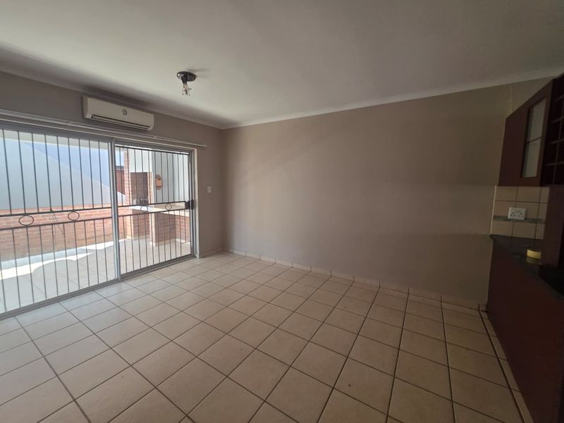 An open-plan living and kitchen area featuring tiled flooring, a split-system air conditioner, and a sliding door leading to an outdoor patio space.