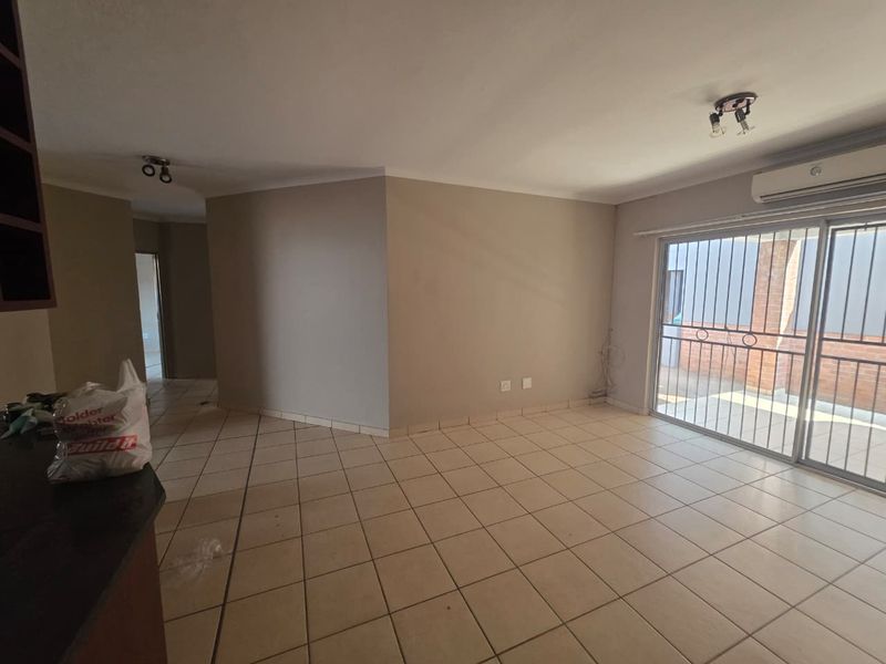 Spacious open-plan living area featuring neutral tiled flooring, a split-system air conditioner, and large sliding glass doors with security gates leading to the exterior.