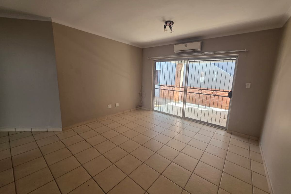 An empty living room featuring ceramic floor tiles, a wall-mounted air conditioning unit, and a sliding glass door with an integrated security gate.