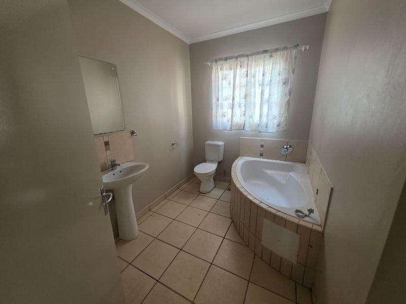 A functional bathroom featuring a corner bathtub, pedestal basin, and toilet with neutral wall tones and tiled flooring.