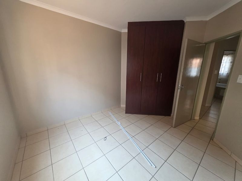 An empty bedroom featuring tiled flooring, neutral walls, and a dark wood built-in wardrobe, with a view into the adjacent hallway.