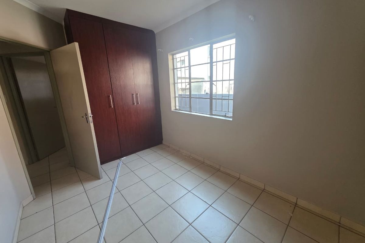 An empty bedroom featuring tiled flooring, built-in wooden cupboards, and a window fitted with security bars.