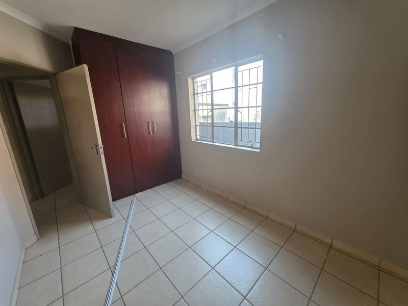 An empty bedroom featuring tiled flooring, built-in wooden cupboards, and a window fitted with security bars.