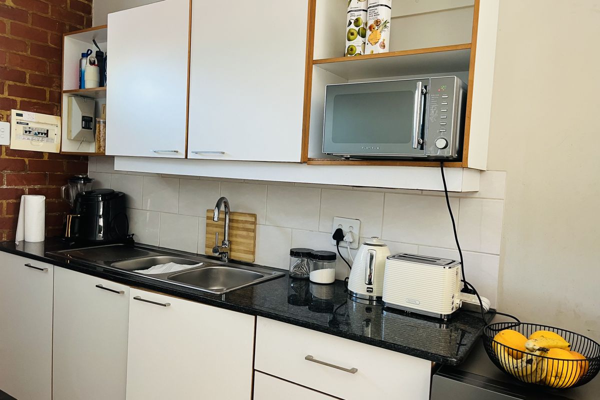 A functional kitchen featuring granite countertops, a double basin sink, white cabinetry, and a characterful exposed brick wall.