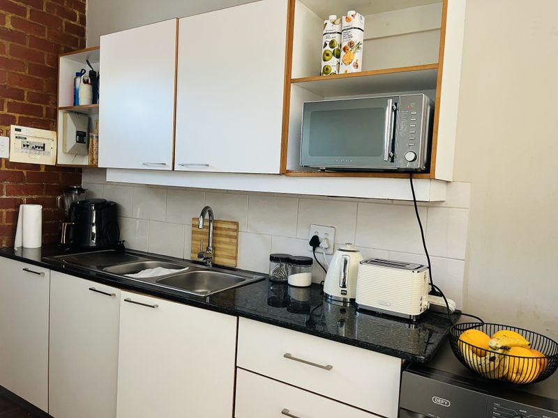 A functional kitchen featuring granite countertops, a double basin sink, white cabinetry, and a characterful exposed brick wall.