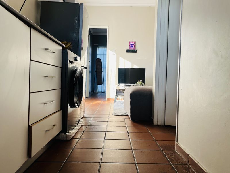 A functional kitchen area featuring tiled flooring and built-in cabinetry with an integrated washing machine, leading into an adjacent living space.