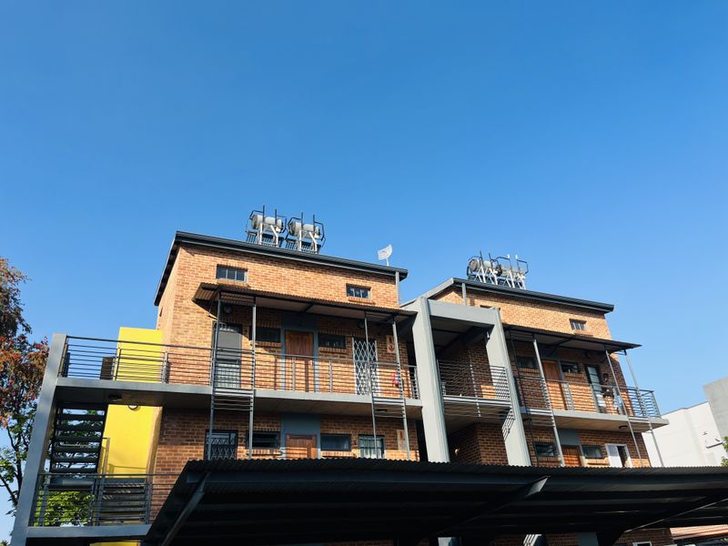 Front elevation of a multi-story brick apartment building featuring external metal staircases, balconies, and a covered carport area.