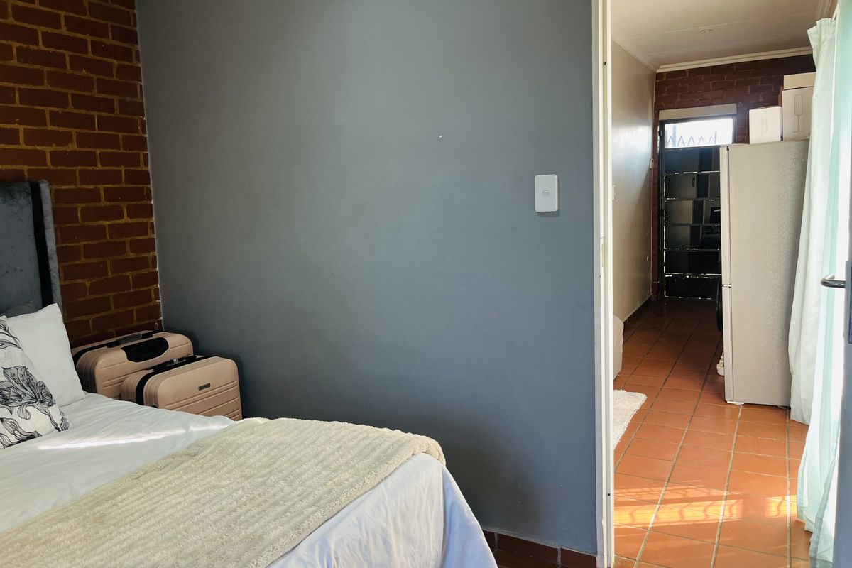 Bedroom featuring an exposed brick feature wall and terracotta floor tiles, with an open doorway leading to an adjacent tiled living area.