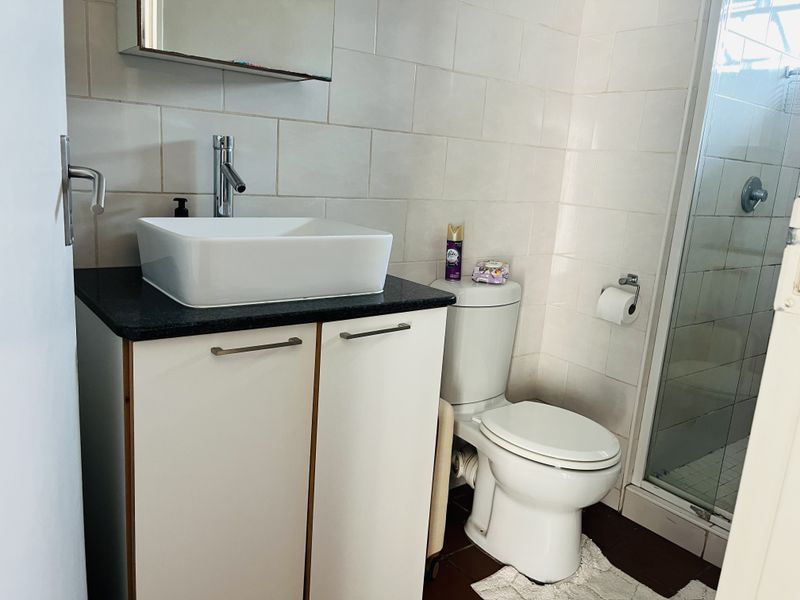 Compact bathroom featuring a modern vessel sink on a granite vanity, a standard toilet, and a glass-enclosed shower with tiled walls.