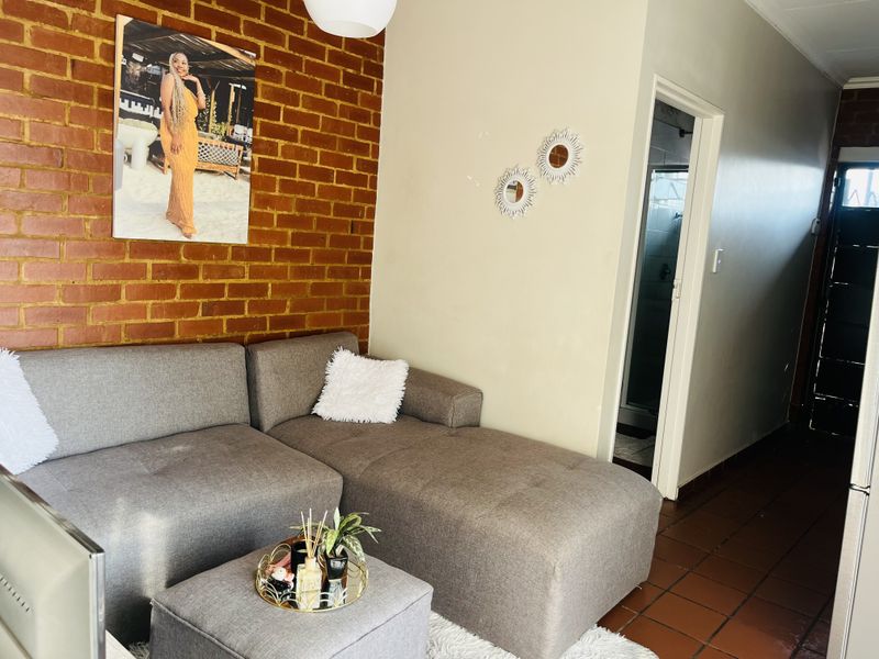 A living room featuring an exposed brick feature wall and tiled flooring, with an adjacent doorway leading to a bathroom area.
