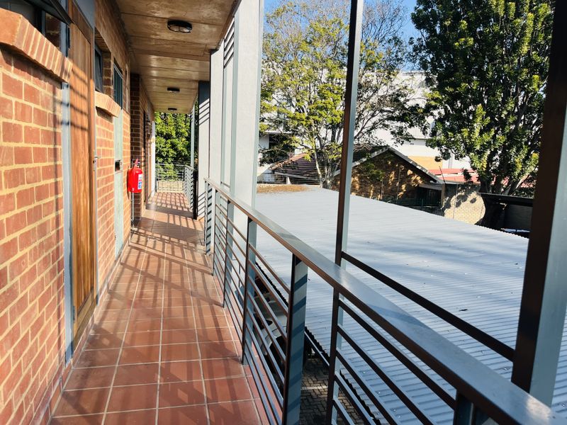 A covered outdoor balcony featuring exposed brick walls, tiled flooring, and a metal balustrade overlooking the surrounding property grounds.