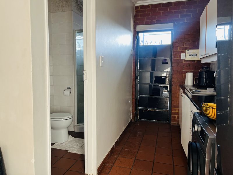 A compact kitchen area featuring exposed brickwork and tiled flooring, with direct access to an adjacent bathroom and an external security door.