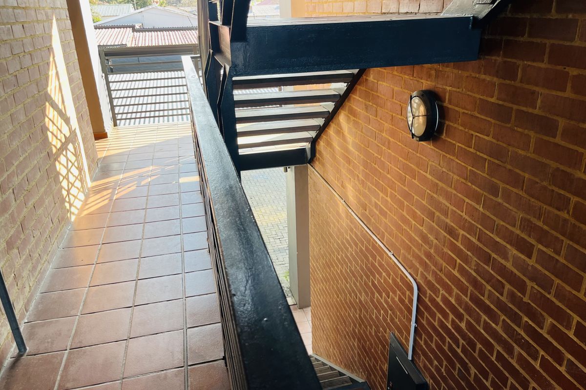 An exterior walkway featuring exposed brick walls, tiled flooring, and a metal staircase leading to the ground level.