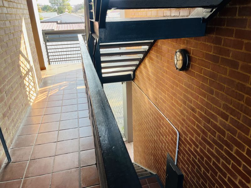 An exterior walkway featuring exposed brick walls, tiled flooring, and a metal staircase leading to the ground level.