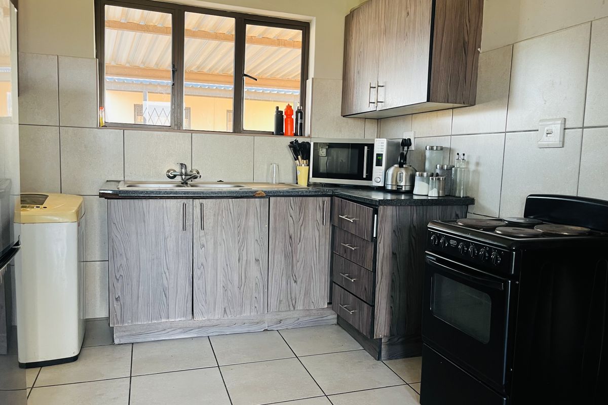 A functional kitchen featuring wood-grain laminate cabinetry, tiled splashbacks, a stainless steel sink, and a freestanding electric stove.
