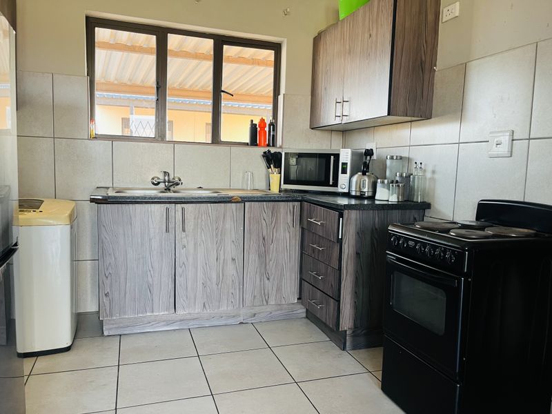 A functional kitchen featuring wood-grain laminate cabinetry, tiled splashbacks, a stainless steel sink, and a freestanding electric stove.