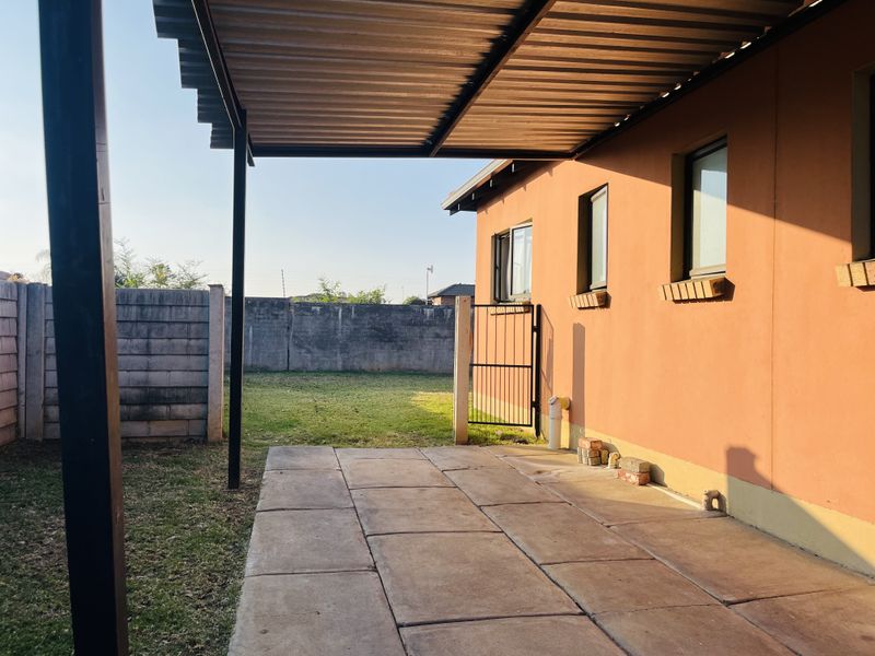 A covered outdoor patio area featuring paved flooring and a metal roof structure, overlooking a private backyard with perimeter walling.