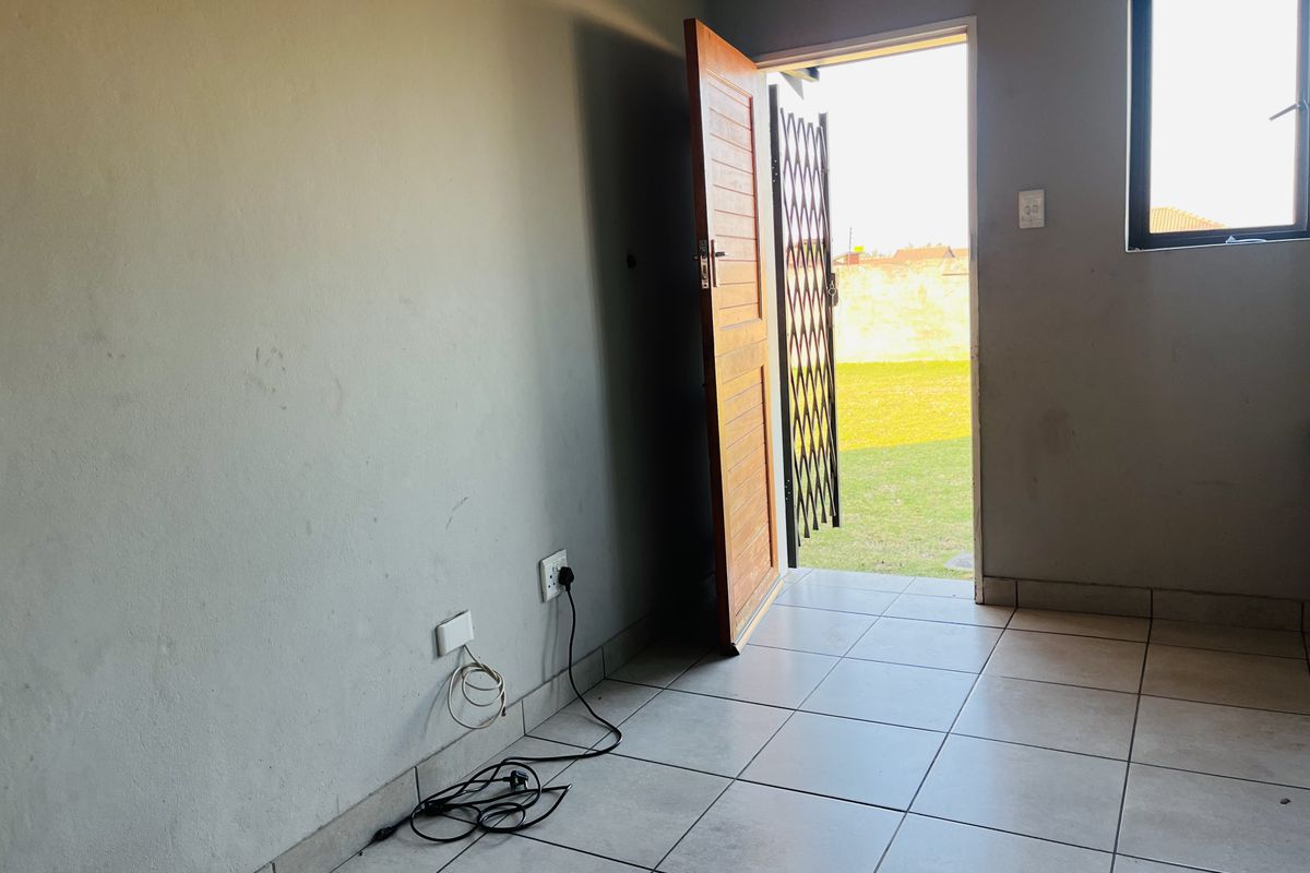 An empty living area featuring tiled flooring, a security gate, and direct access to the outdoor garden space.
