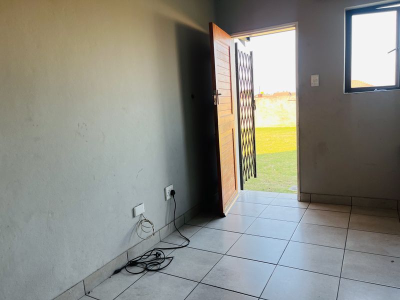 An empty living area featuring tiled flooring, a security gate, and direct access to the outdoor garden space.