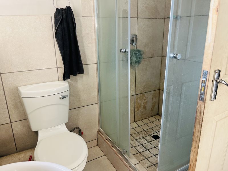 A compact bathroom featuring a standard toilet and a glass-enclosed shower with tiled finishes, showing signs of wear and requiring maintenance.