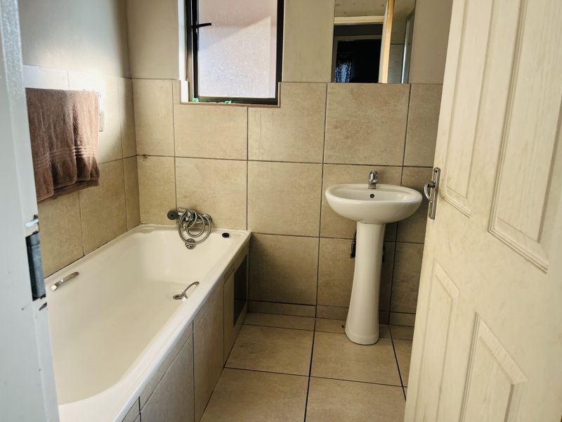 A functional bathroom featuring a pedestal basin, built-in bathtub, and neutral wall and floor tiling.