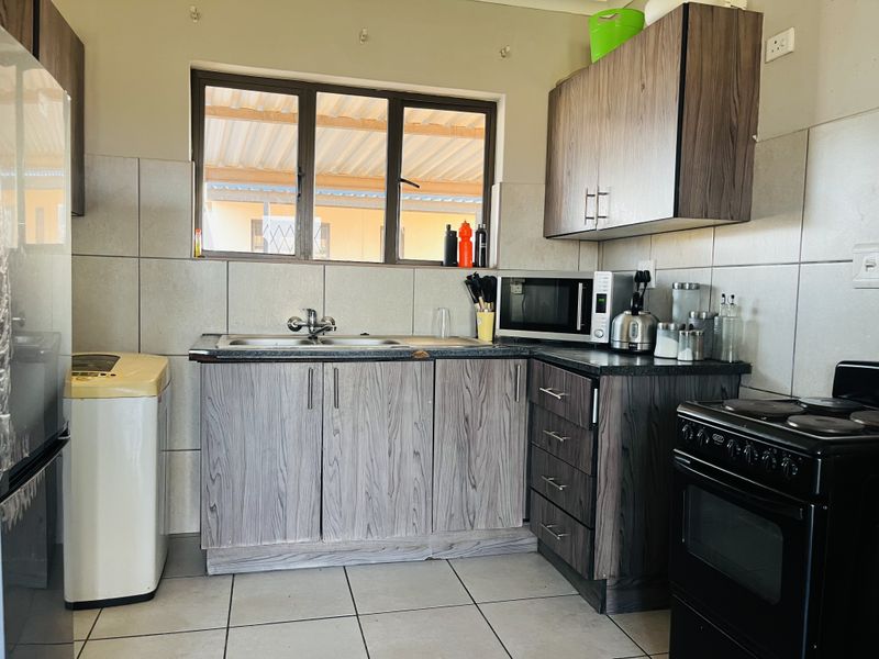 Functional kitchen featuring wood-look cabinetry, tiled splashbacks, double sink, and space for a freestanding stove and laundry appliance.