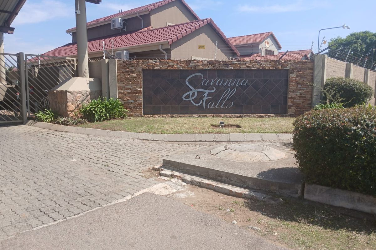 Entrance view of Savanna Falls residential estate featuring a stone-clad signage wall, paved driveway, and secure perimeter fencing.