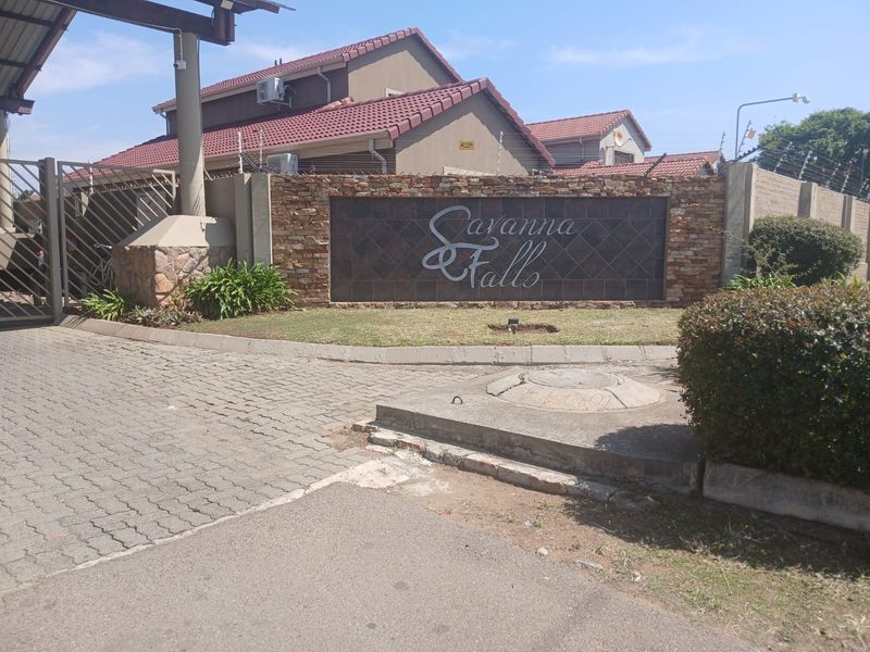 Entrance view of Savanna Falls residential estate featuring a stone-clad signage wall, paved driveway, and secure perimeter fencing.