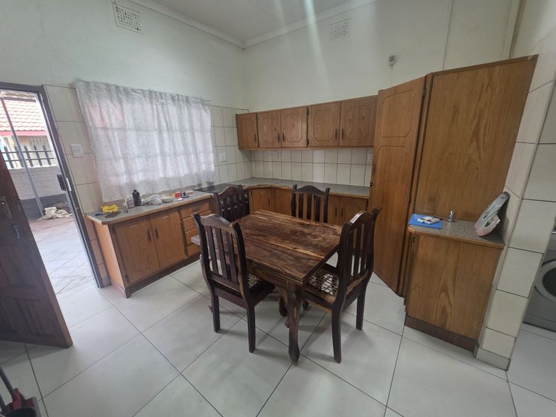 A functional kitchen featuring traditional wooden cabinetry, tiled splashbacks, and tiled flooring with direct access to an outdoor area.