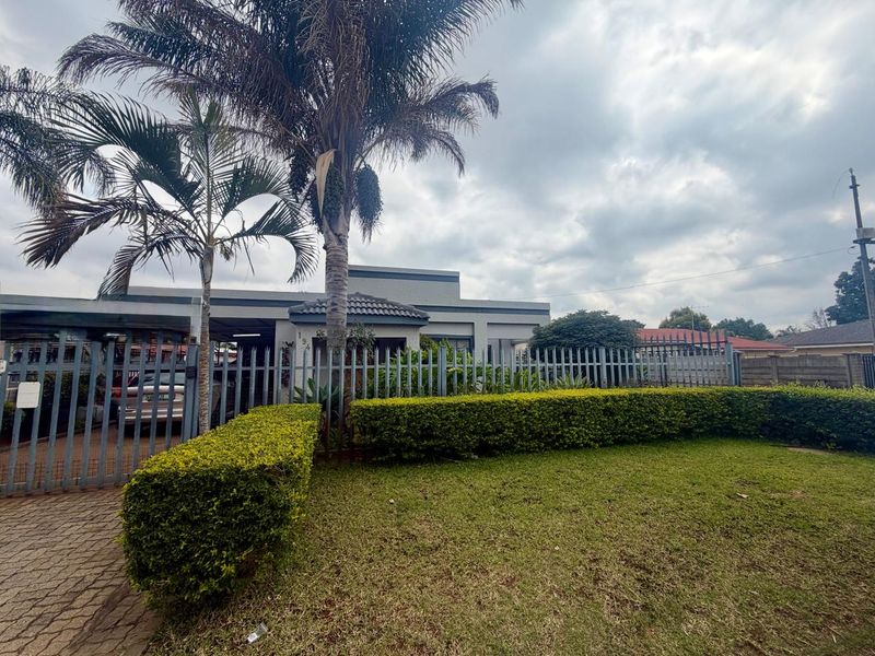 Front view of the property featuring a paved driveway, steel palisade fencing, and a well-maintained garden hedge.