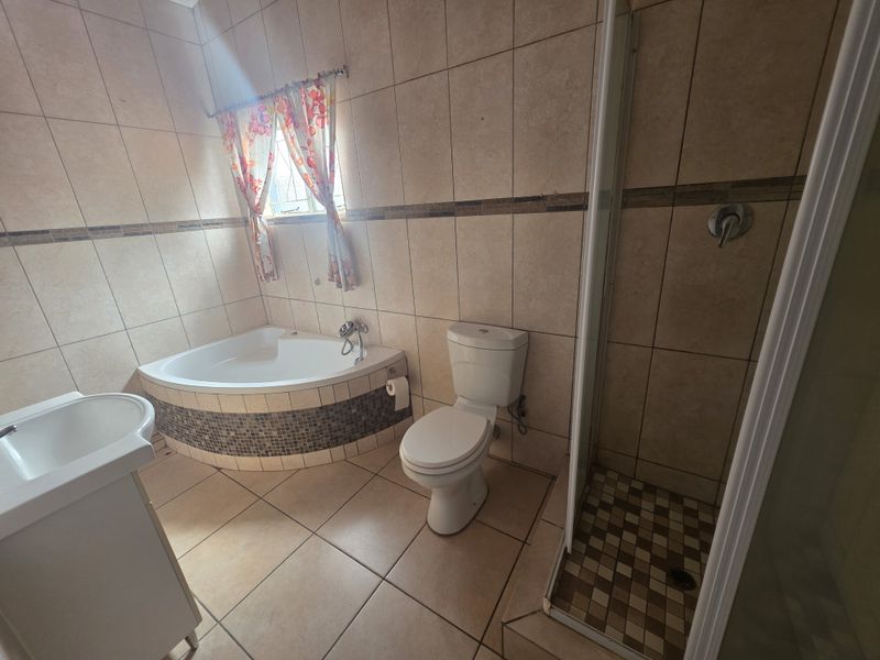 A functional bathroom featuring a corner bathtub, separate shower enclosure, pedestal basin, and toilet with neutral wall and floor tiling.
