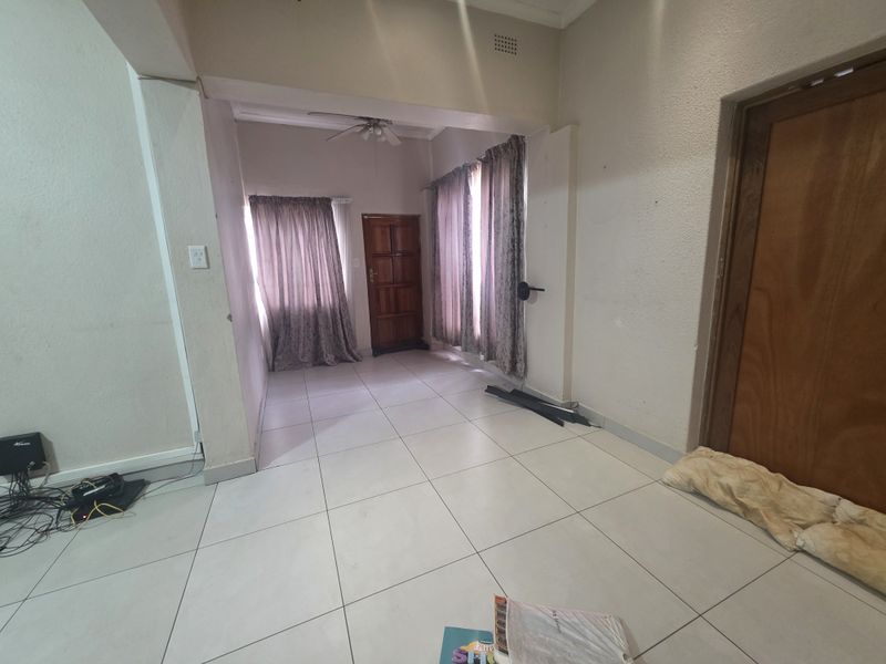 An empty living area featuring tiled flooring, a ceiling fan, and wooden door access, providing a blank canvas for interior design.