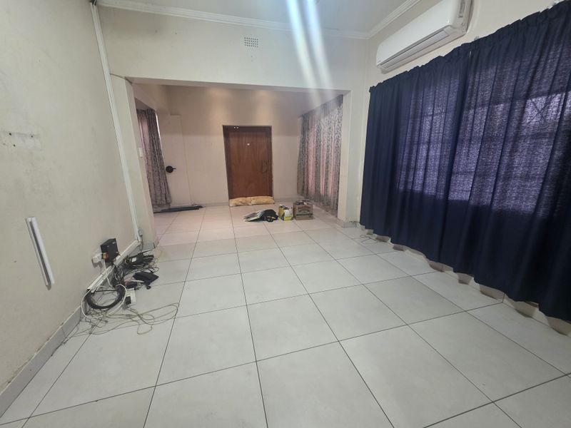 An open-plan living area featuring neutral tiled flooring, a wall-mounted air conditioning unit, and a timber entrance door.