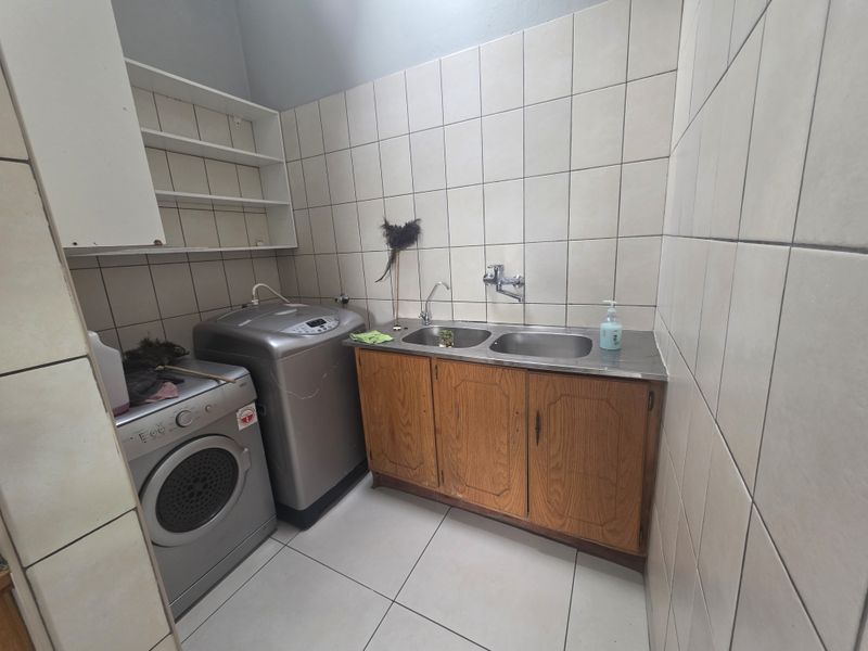 Functional laundry room featuring a double stainless steel sink, built-in wooden cabinetry, wall-mounted shelving, and full-height ceramic wall tiling.