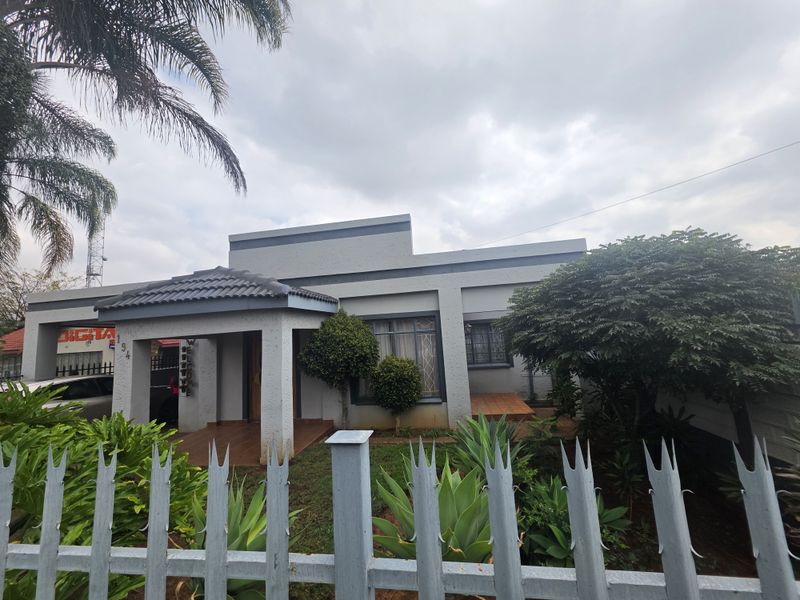Front elevation of a single-story house featuring a covered entrance porch, tiled roof, and secure perimeter fencing with metal spikes.