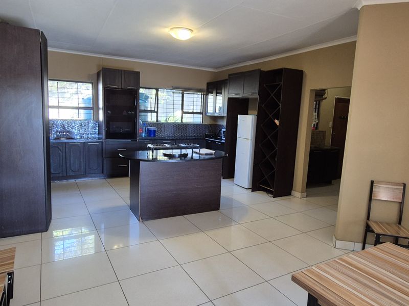 Spacious kitchen featuring dark wood cabinetry, granite countertops, a central island, and tiled flooring, offering a functional layout with ample storage.