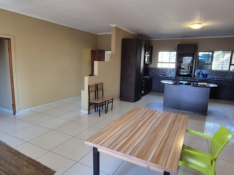 Open-plan living and kitchen area featuring tiled flooring, dark cabinetry, a central kitchen island, and built-in cooking appliances.