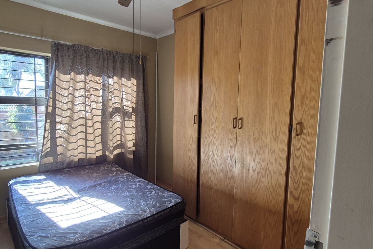 A bedroom featuring built-in wooden cupboards, a ceiling fan, and security bars on the window.