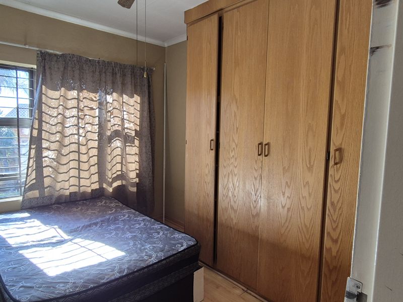 A bedroom featuring built-in wooden cupboards, a ceiling fan, and security bars on the window.