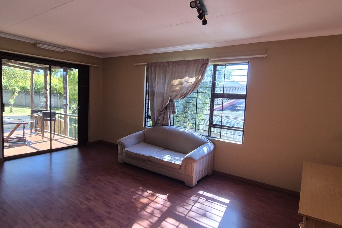 Spacious living room featuring laminate flooring, large windows with security bars, and a sliding glass door providing access to the outdoor patio area.