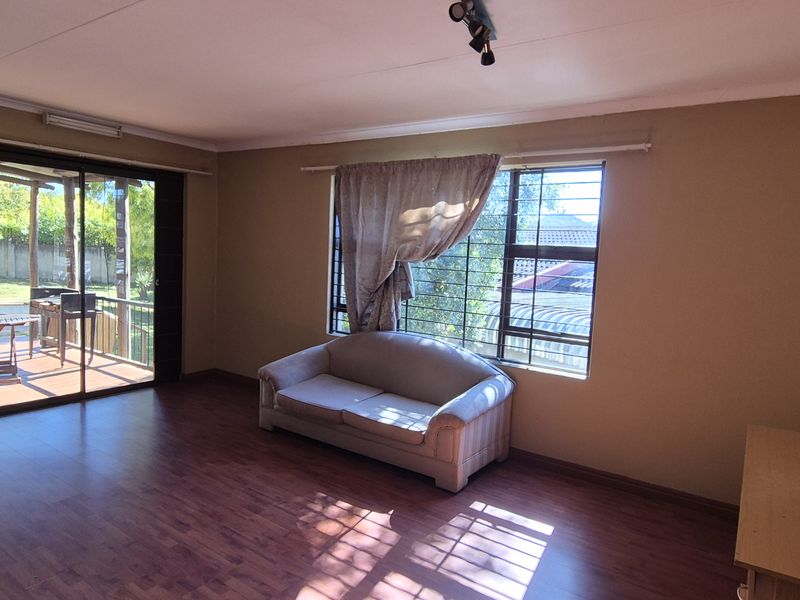 Spacious living room featuring laminate flooring, large windows with security bars, and a sliding glass door providing access to the outdoor patio area.
