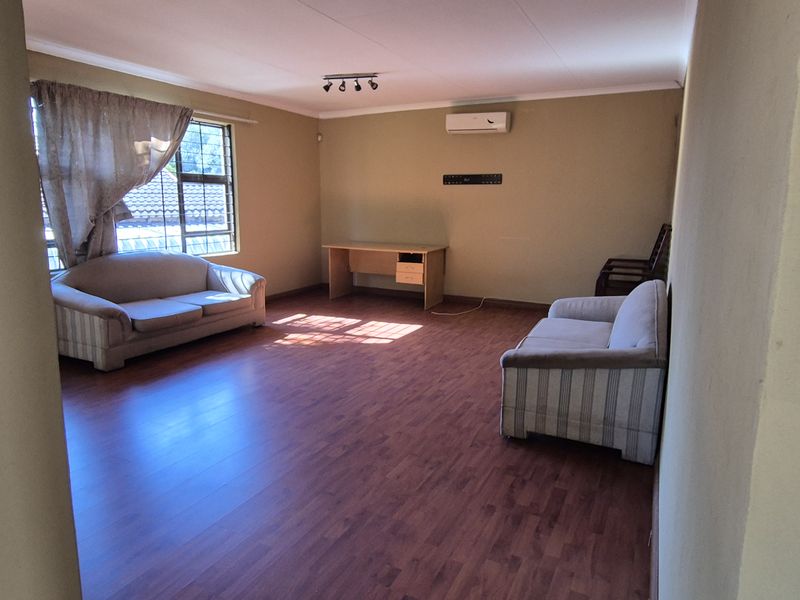 Spacious living room featuring laminate flooring, coving, and a wall-mounted air conditioning unit, offering a comfortable and functional living space.
