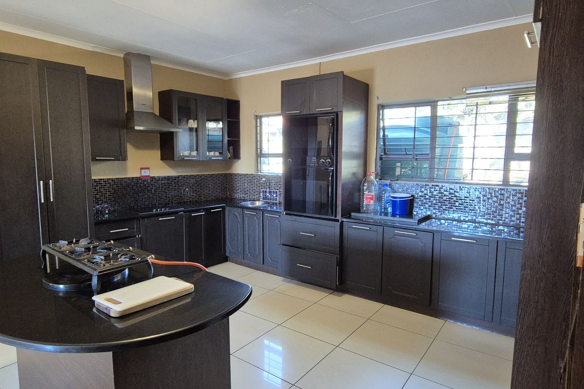 A functional kitchen featuring dark wood cabinetry, granite countertops, a mosaic tile backsplash, and tiled flooring with integrated storage and an extractor fan.